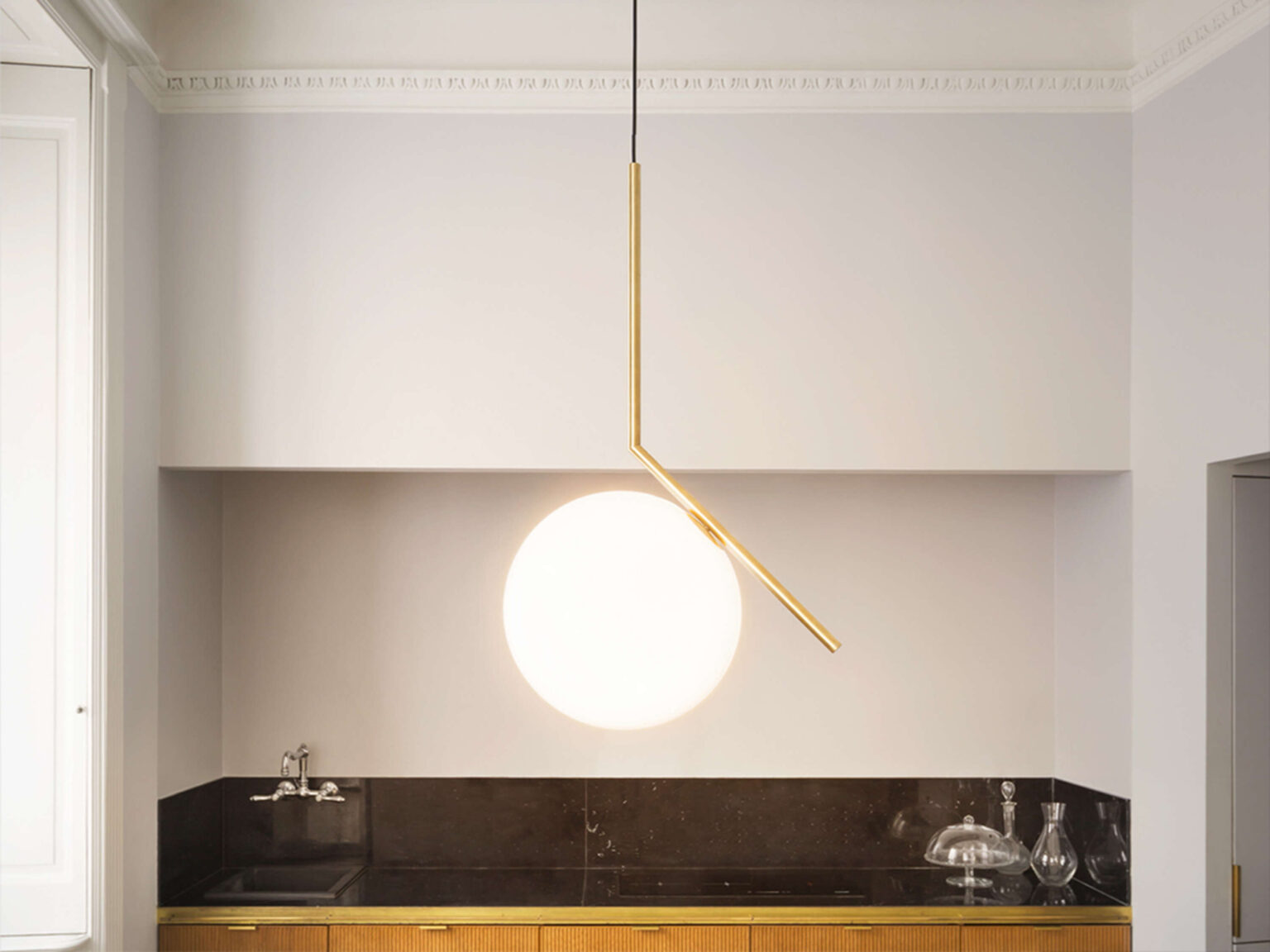 Black‑framed IC Lights S1 pendant over a bedroom side table, casting warm diffused light through its opal globe.