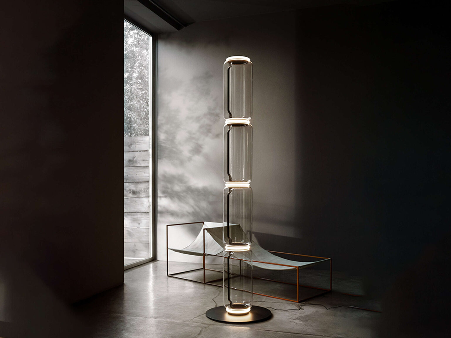 Noctambule lamp in a dimly lit room, its cylindrical glass units softly illuminated with integrated LED at top and bottom.