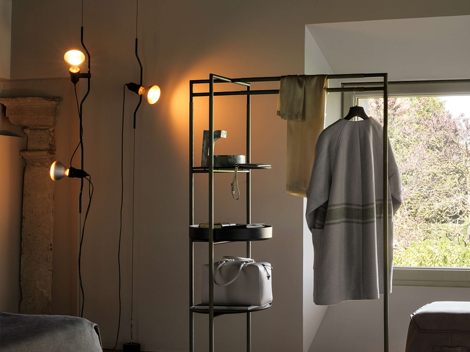 Parentesi lamp head sliding vertically along its steel cord, highlighted against a white wall with subtle shadows.