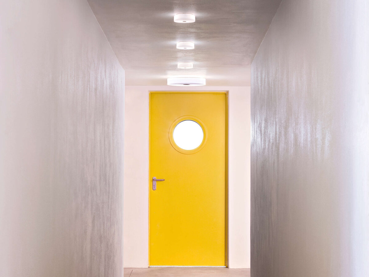 A contemporary Flos Mini Button light in white, showcasing its clean, button-like form (14cm diameter), ideal for blending into modern residential or commercial spaces, including damp locations.