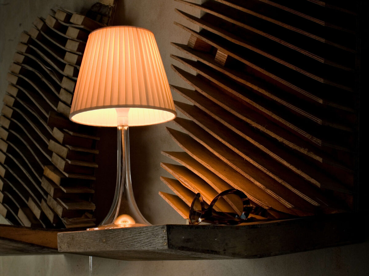 Modern table lamp with a translucent outer shell and warm glow, Miss K by Flos on a bedside table.
