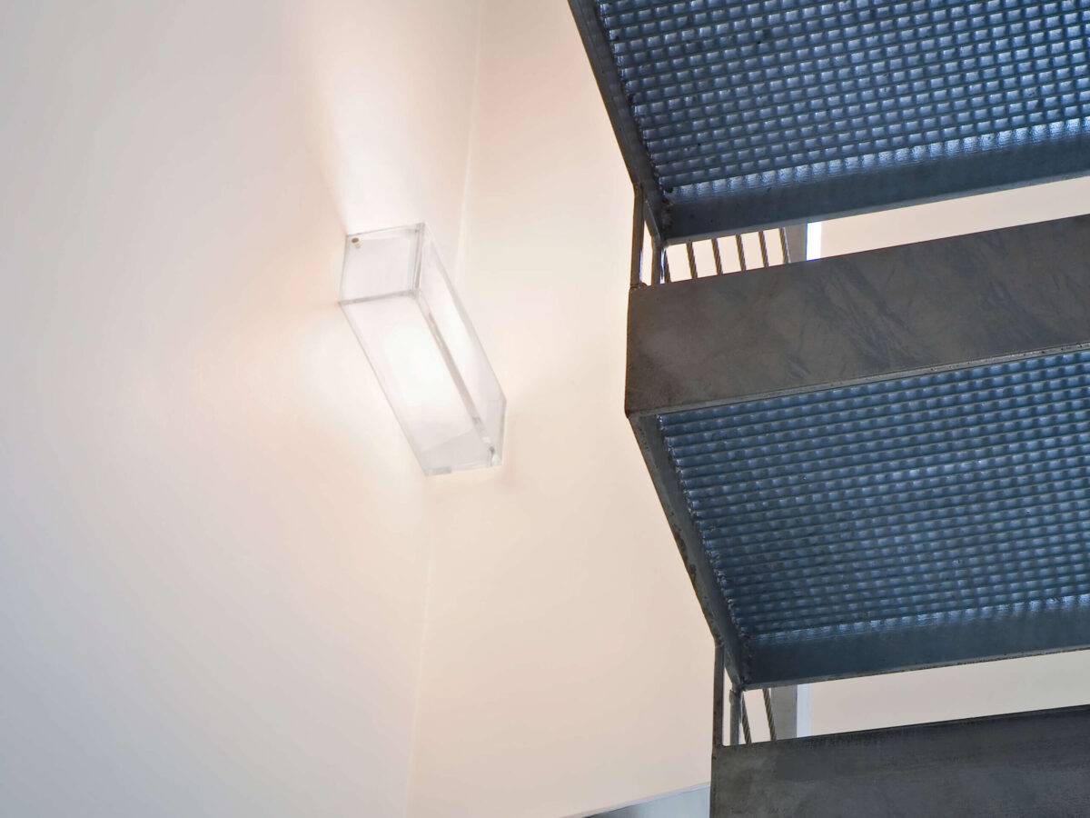 An elegant Flos Ontherocks HL wall fixture, composed of clear molded glass with a subtle internal white diffuser, mounted on a white powder-coated aluminum wall plate, offering direct and indirect light.