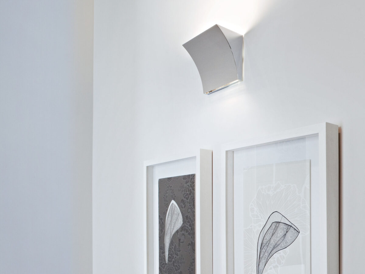 A minimalist Flos Pochette Up/Down LED lamp, showcasing its clean lines and subtle curved form, with integrated LEDs that illuminate the wall above and below the fixture.