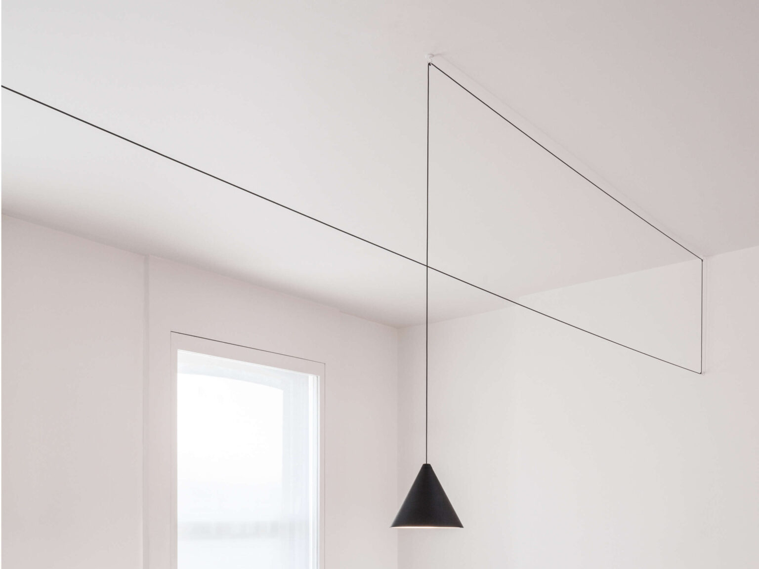 White varnished aluminium cone pendant with 12 m Kevlar-reinforced cable creating a sculptural linear outline across the ceiling.