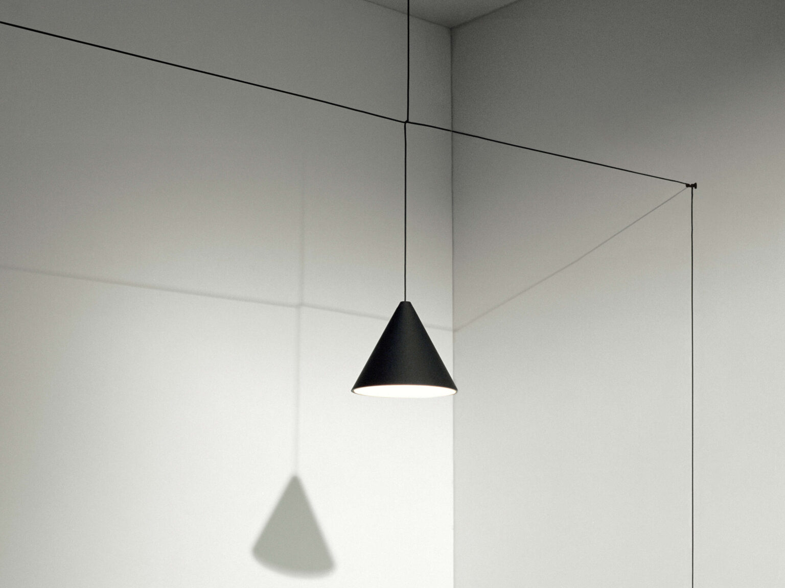 Blue soft-touch varnished die-cast aluminium cone hanging over a dining table, connected by minimal overhead cables.
