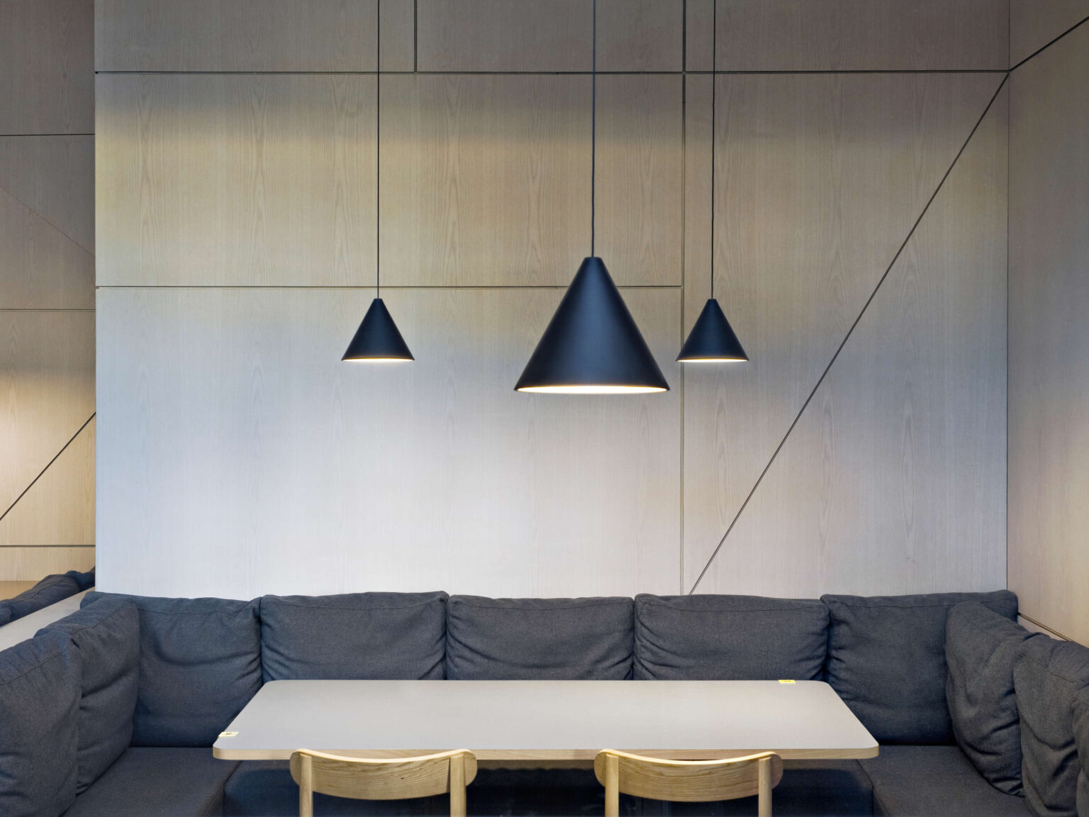Dual String Light Cone pendants in matte black, their cables arranged geometrically in an interior space above seating.