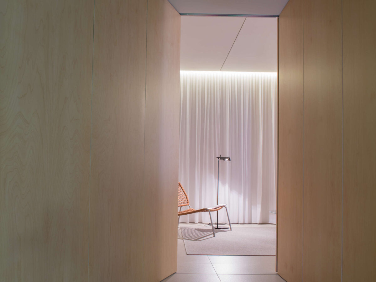 White Tab Floor lamp lit softly in a workspace, its head angled to one side with clear cable rising to ceiling.