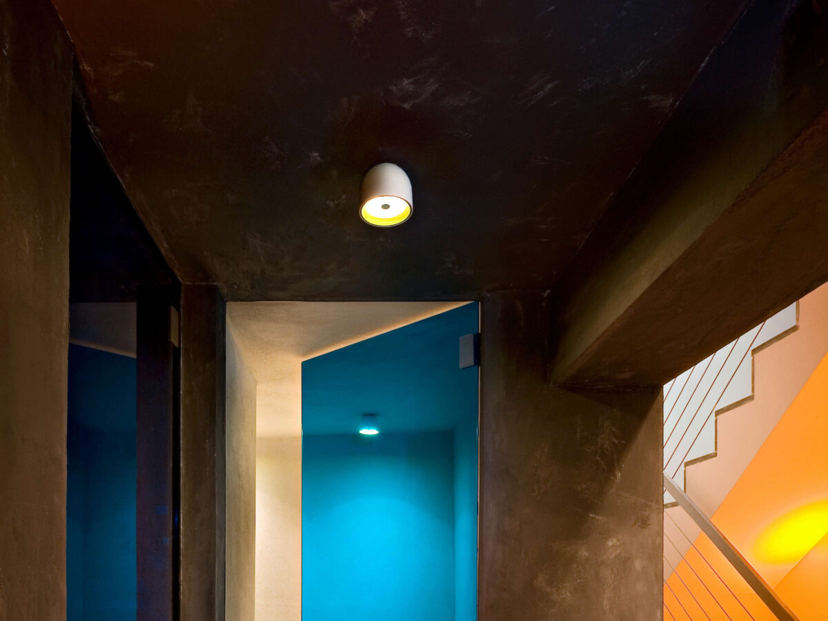 The minimalist Flos Wan C/W light by Johanna Grawunder, a small, circular fixture with a polished aluminum body and an internal anti-glare shield, creating focused illumination.