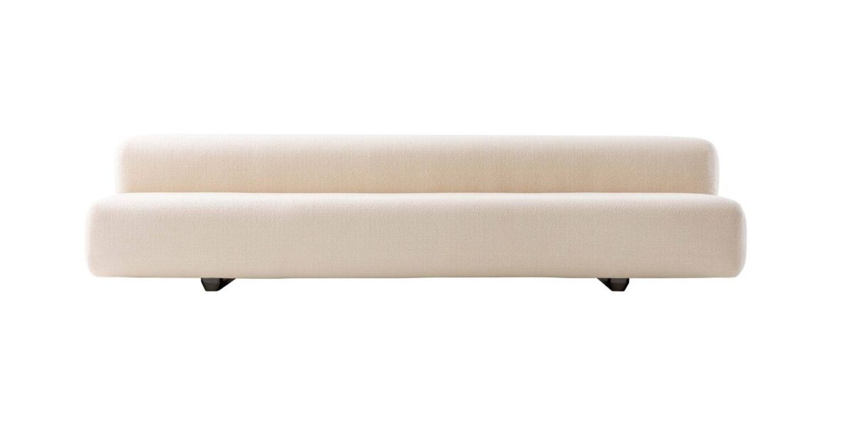 “Three-quarter view of Big Sofa under pergola, its plush upholstery contrasting with polished chrome legs in an outdoor-adjacent lounge setting.”
